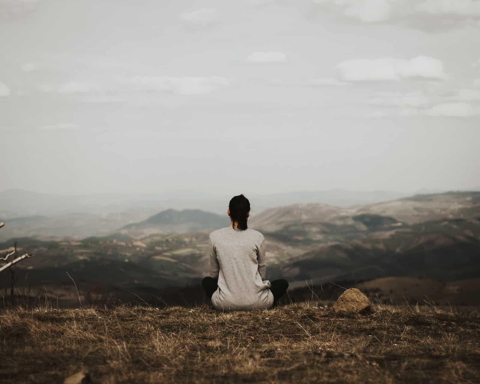 Woman sitting on cliff overlooking mountains during daytime-loneliness after break up