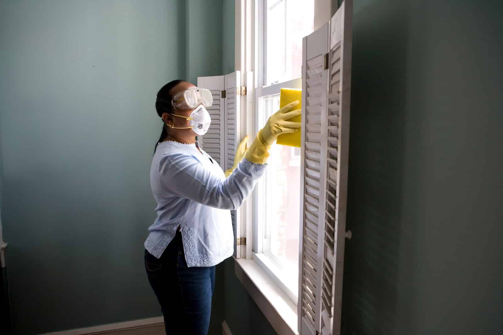 Woman in white long sleeve shirt and blue denim jeans standing beside white wooden framed glass-proven house cleaning hacks