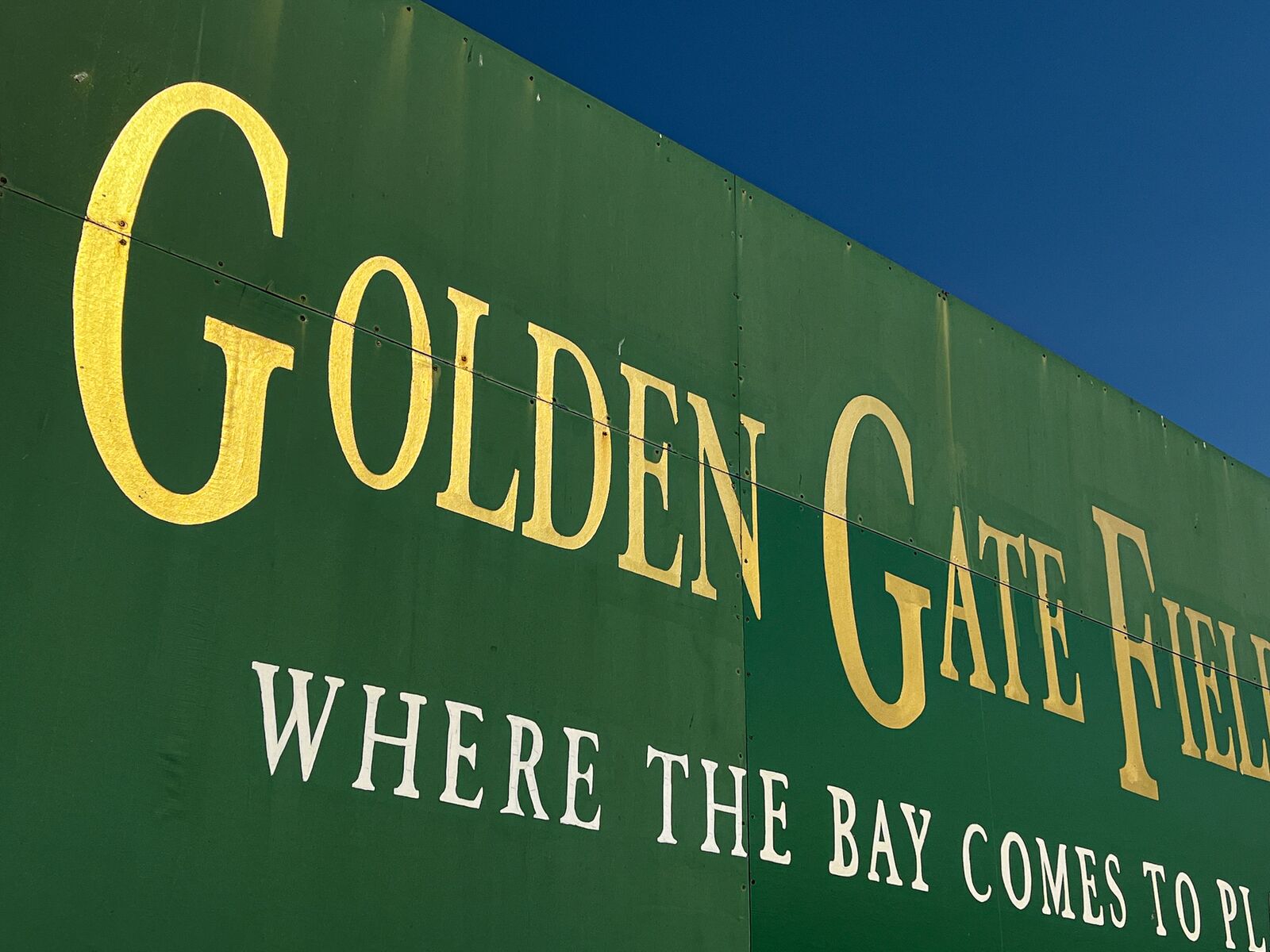 A green sign reads "Golden Gate Fields" in gold letters, with the racetrack's slogan, "where the bay comes to play," beneath it in white.