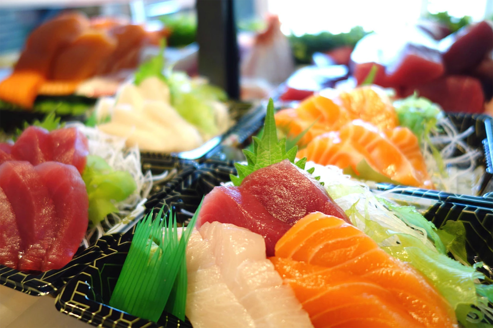 Trays of nigiri style sushi sit inside a display case.