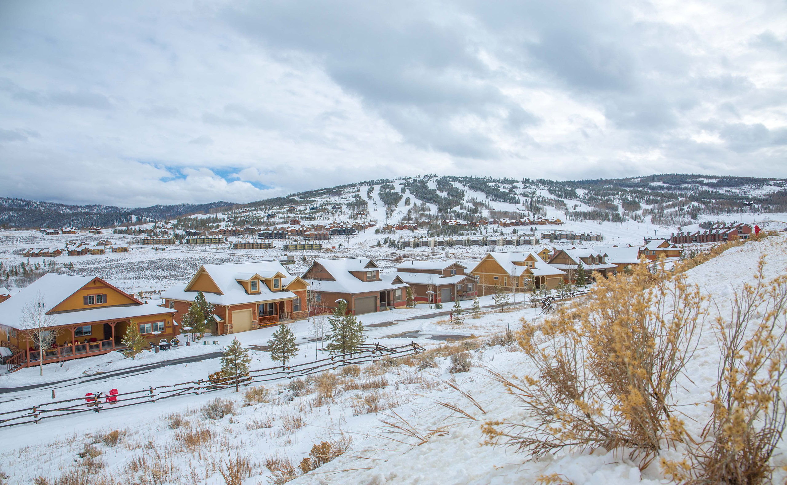 A group of houses in the snow with mountains in the background.