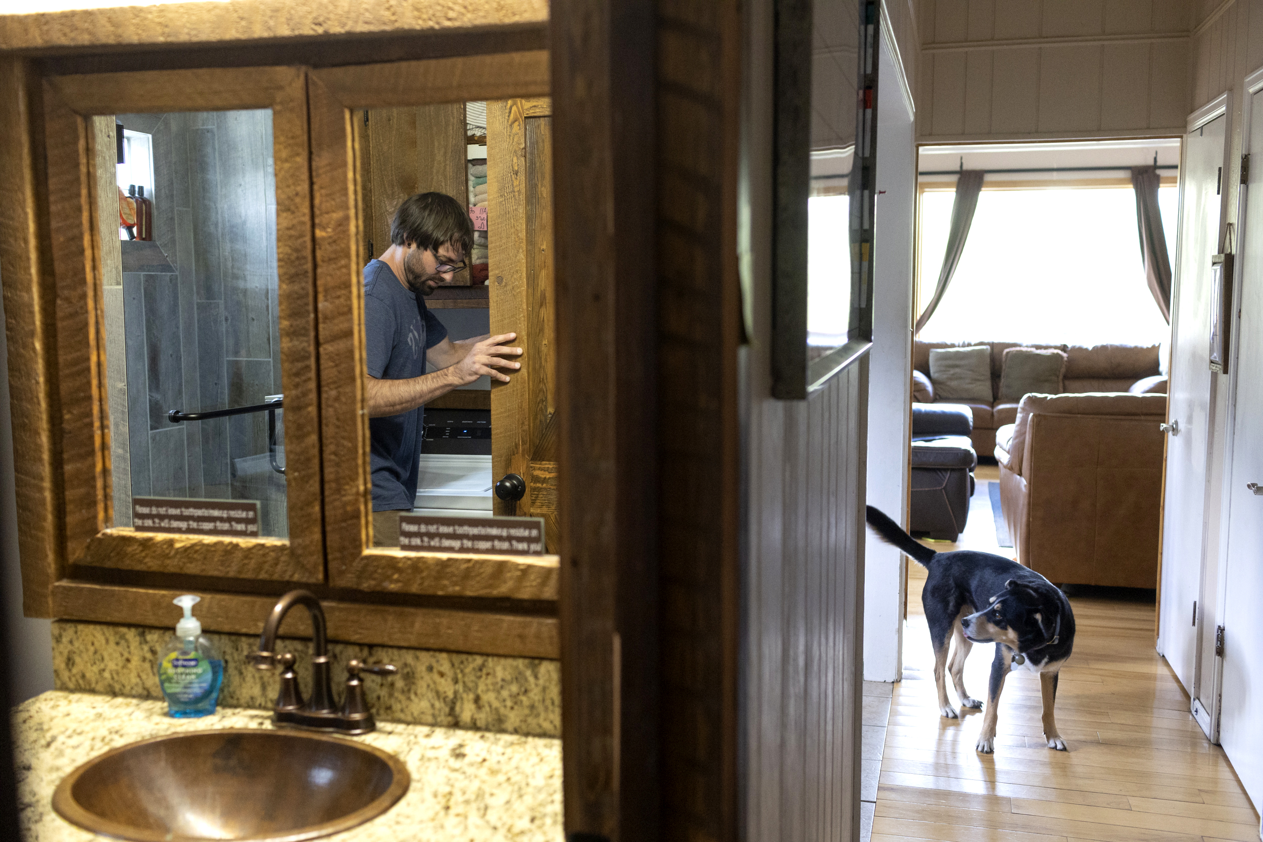 A man does laundry in a bathroom with his dog in hallway.