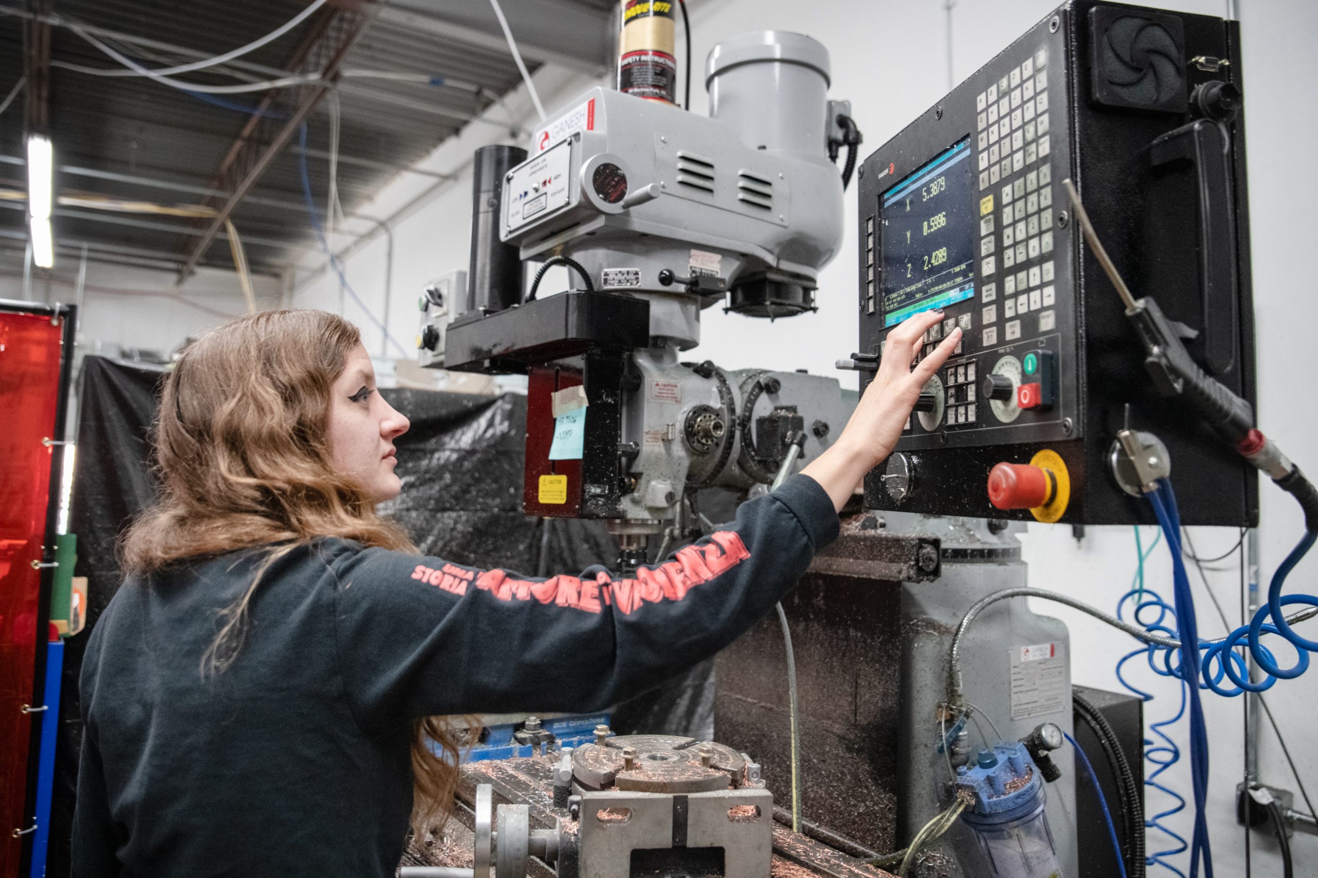 A woman presses buttons on a control panel next to large machinery.