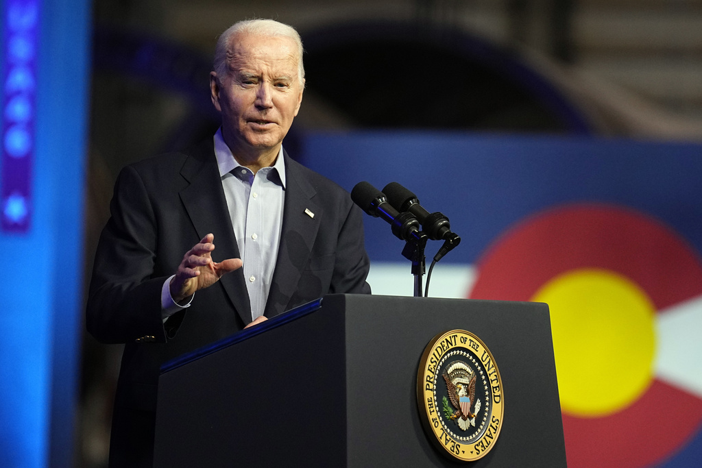 Joe Biden in a suit speaks into microphones on a podium with a presidential seal.