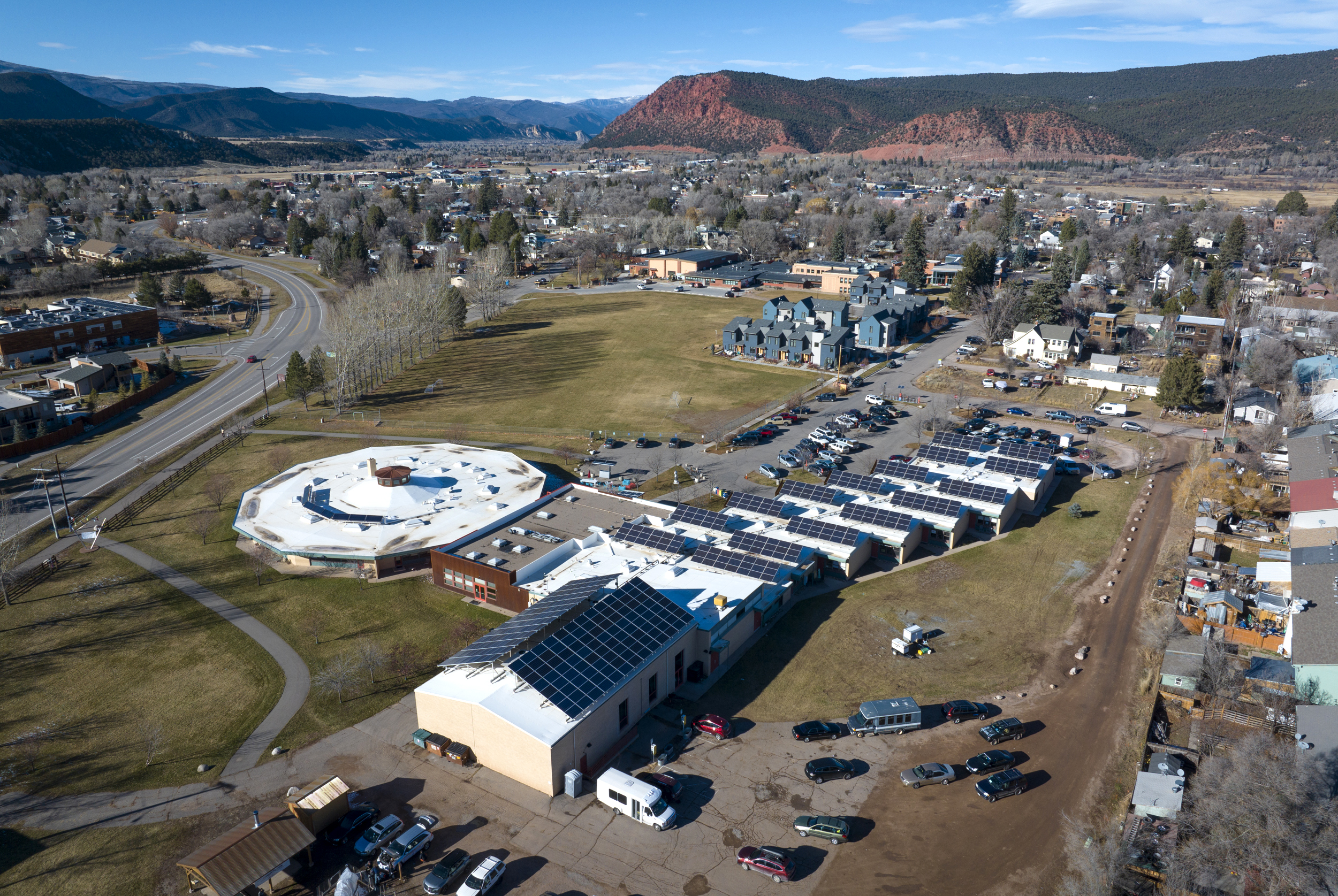 Aerial overview of a building with solar panels on the roof in a valley filled with homes