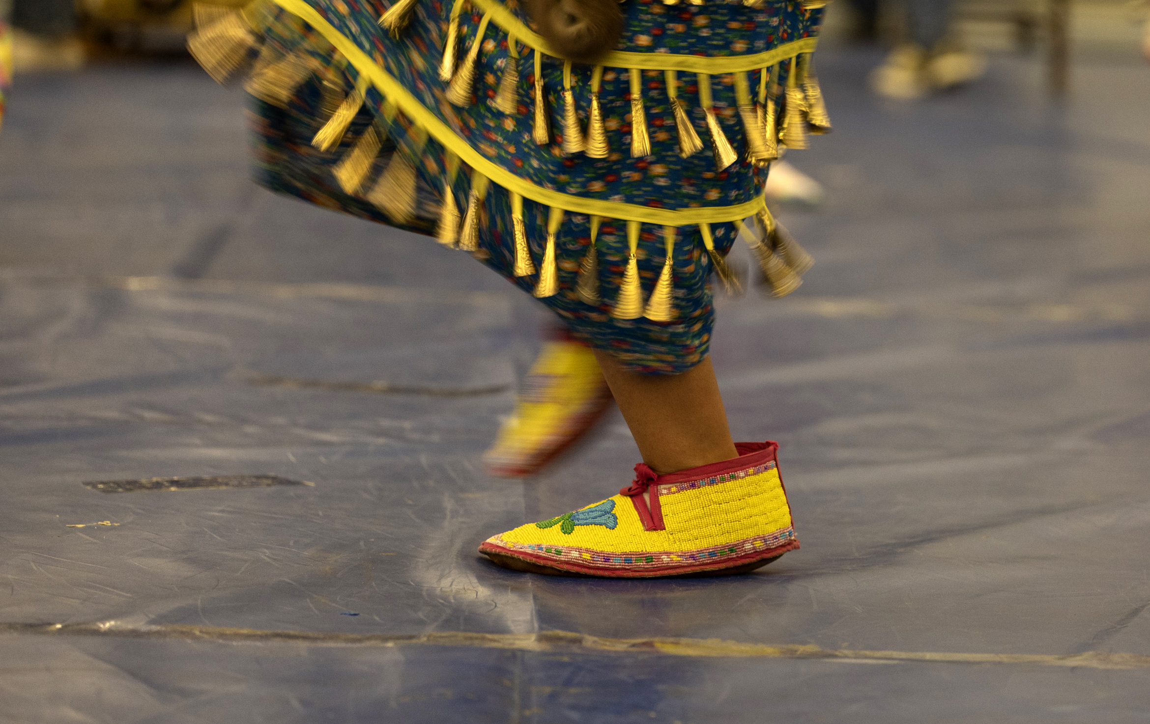 A close-up of the dancing feet of a woman in Native American regalia in a gym