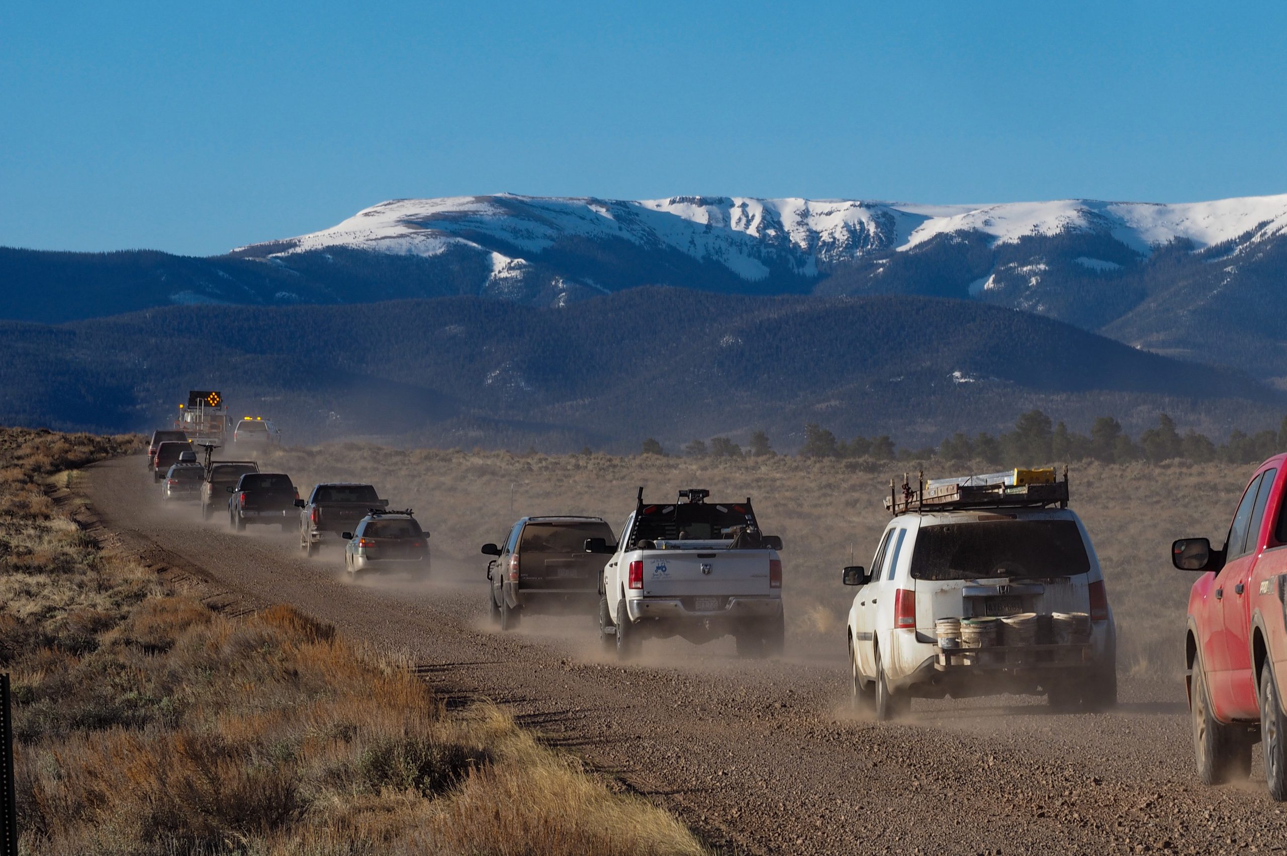 Cars and work trucks drive along a dirt road, including one loaded down with painting supplies