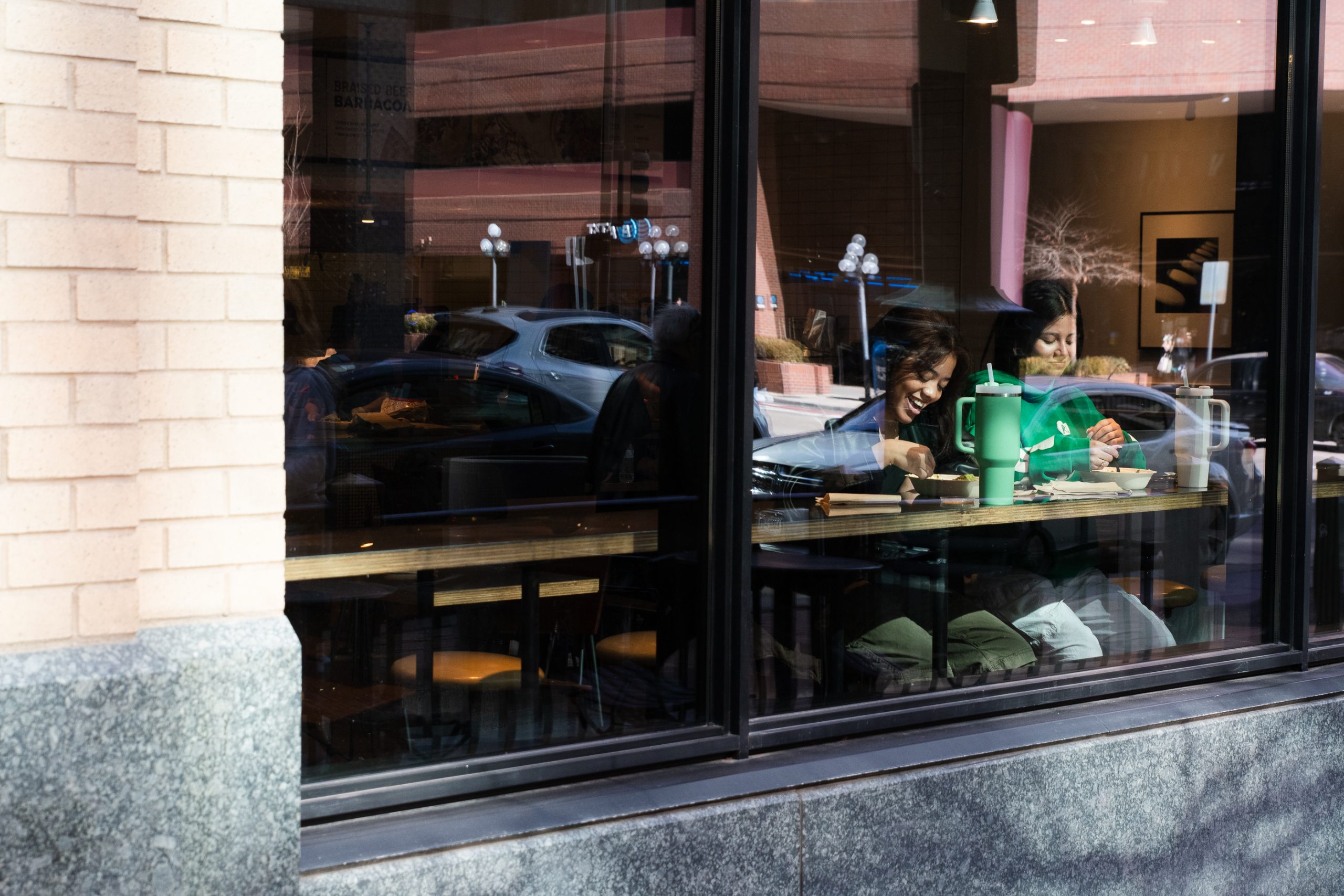 A photo through a window shows to people smiling while eating Chipotle.