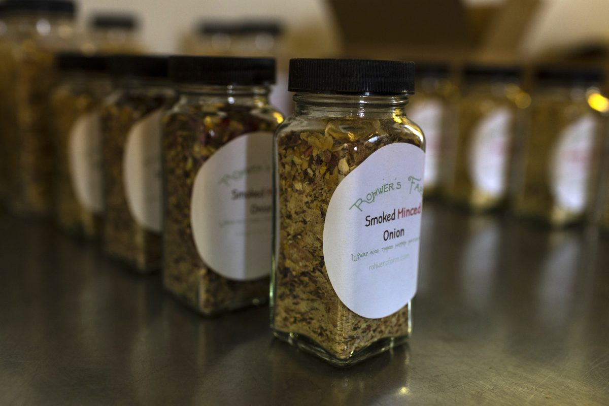 Glass jars with black lids, labeled "Smoked Minced Onion," are lined up on a metallic surface.