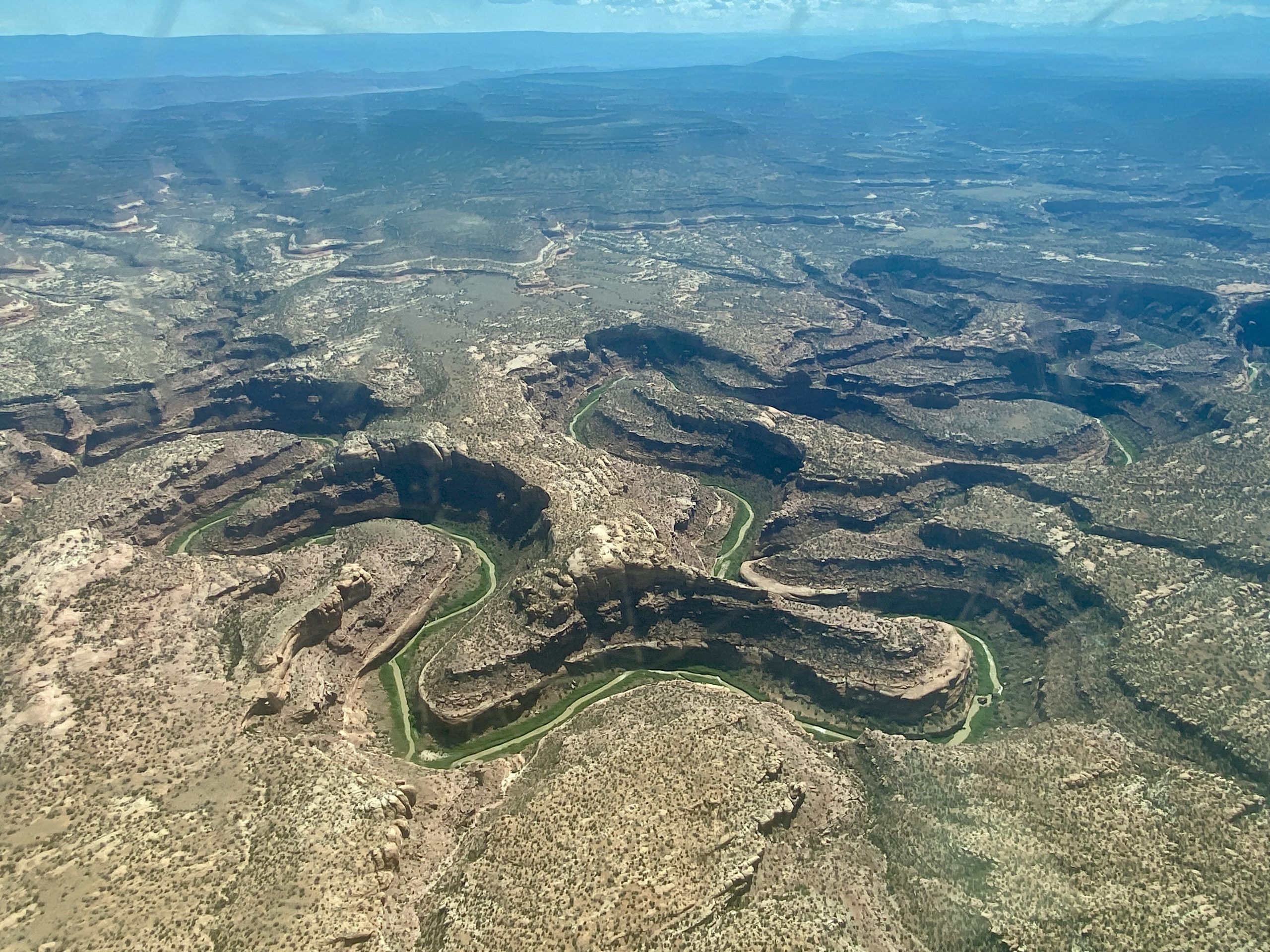 Aerial view of a rugged, winding canyon landscape with a river cutting through the arid terrain under a clear blue sky.