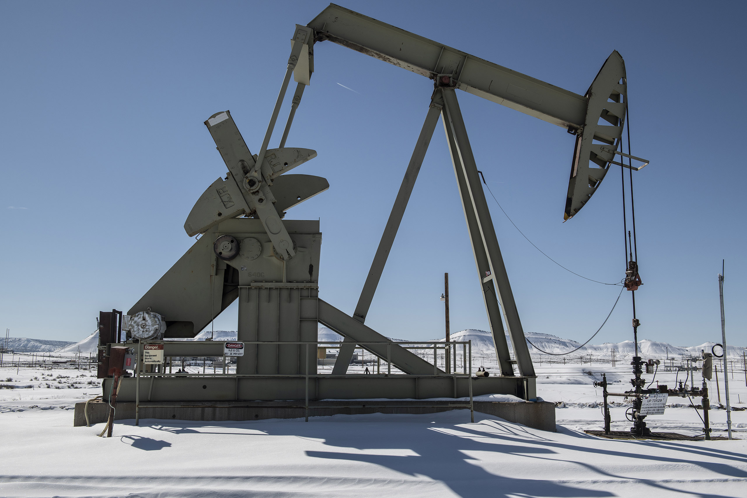 An oil and gas pump jack in a remote area with snow covering the ground.