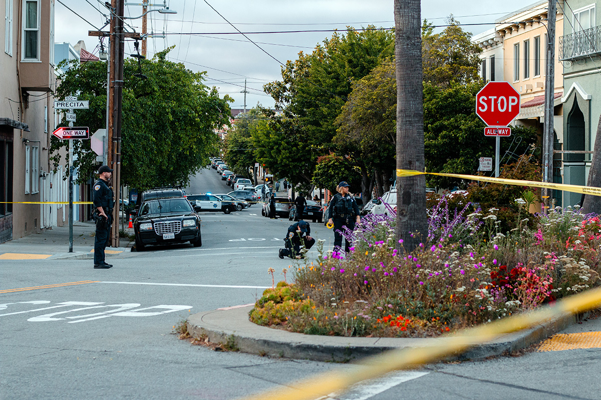 Police standing in the street, yellow tape across the street from a flowered medium