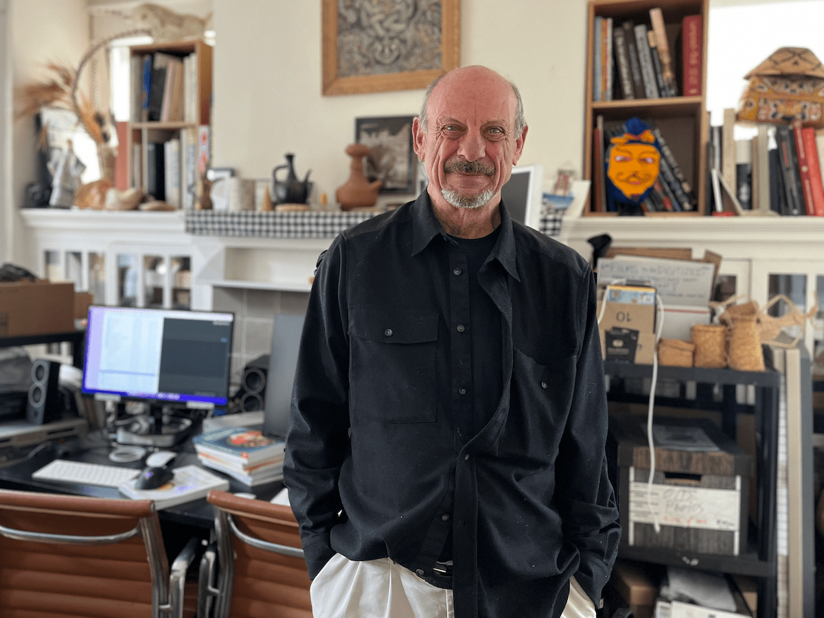 A man stands in front of a cluttered desk and mantel.