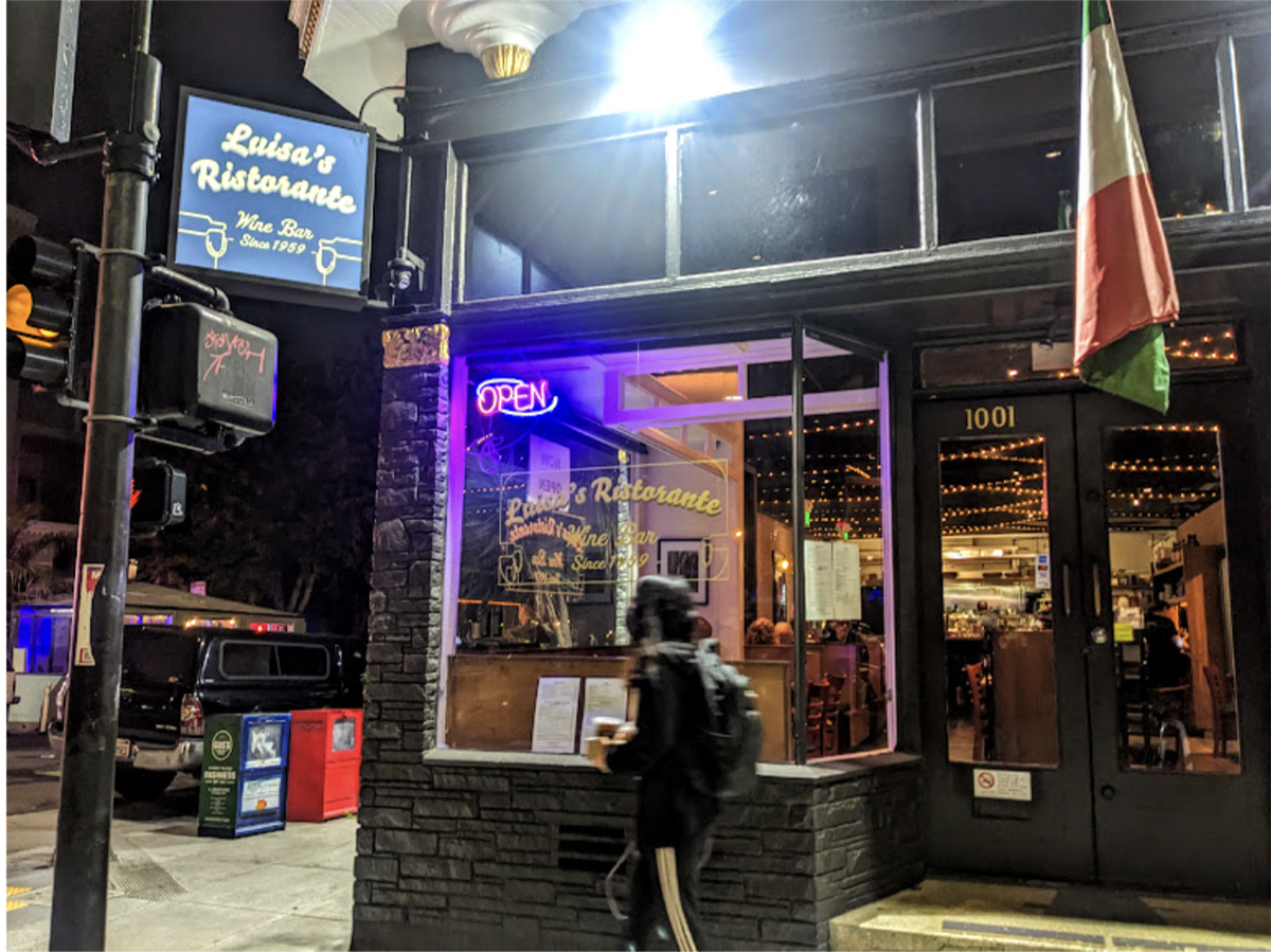 A woman walks past a restaurant at night.