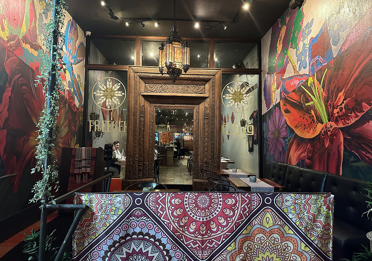 Elegant restaurant interior with vibrant floral murals and ornate wooden door.