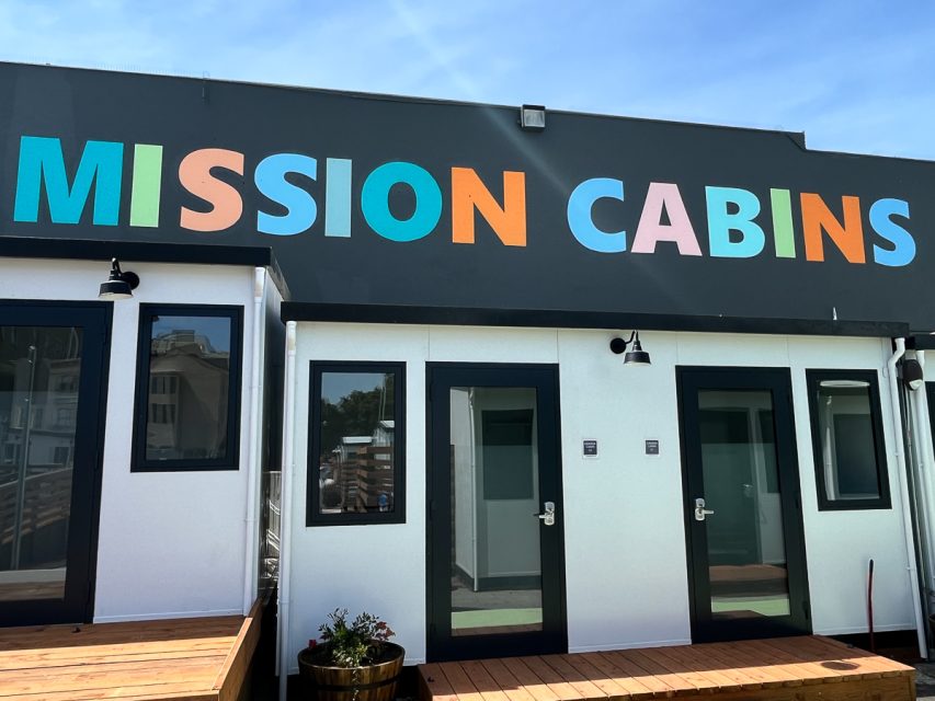 A row of modern white cabins with colorful "mission cabins" signage above the entrance doors, under a clear blue sky.