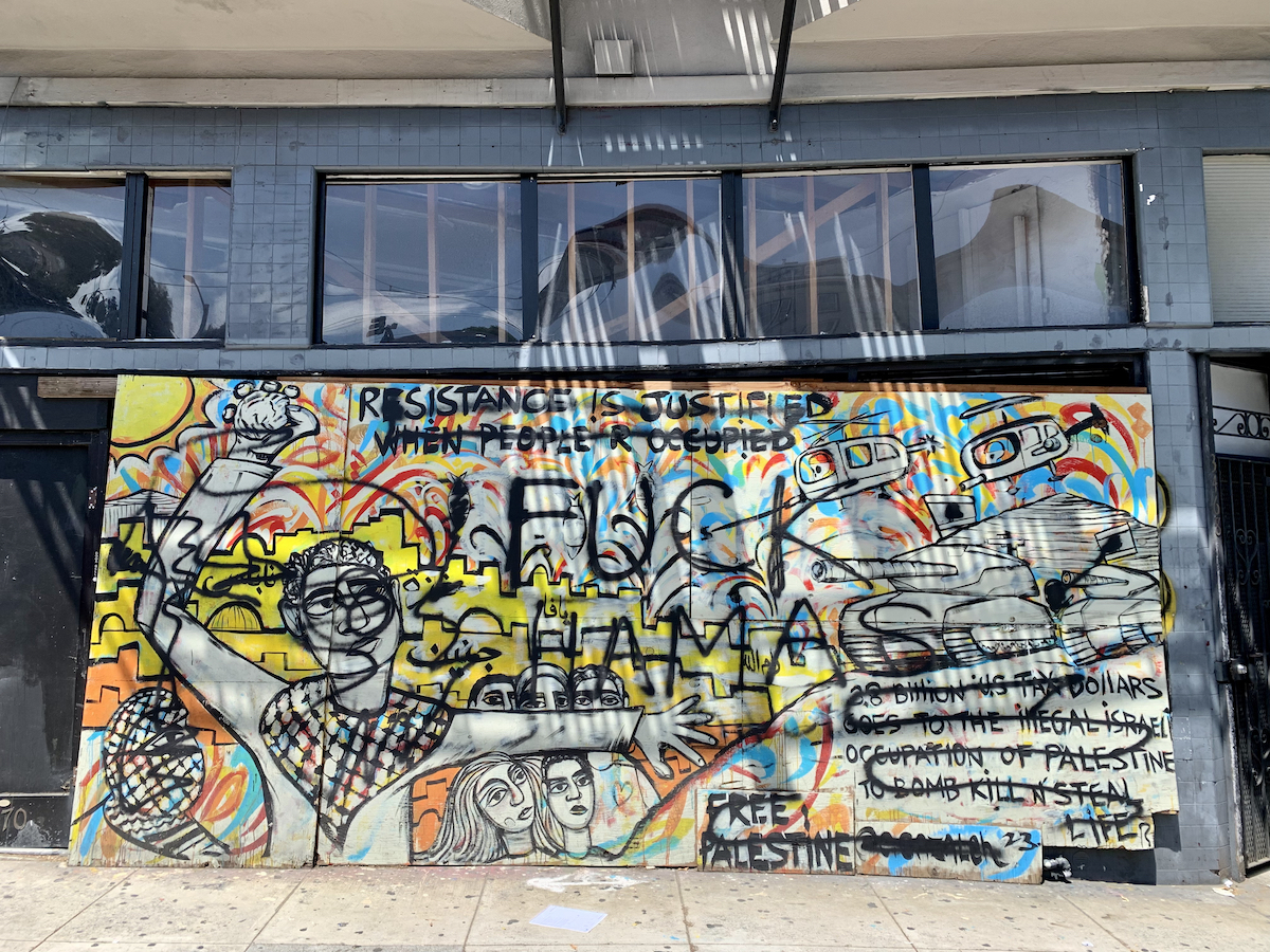 A colorful mural on a building depicts scenes supporting Palestine, with the phrases "Resistance is justified when people are occupied" and "Free Palestine." The mural includes various drawings and symbolic elements.