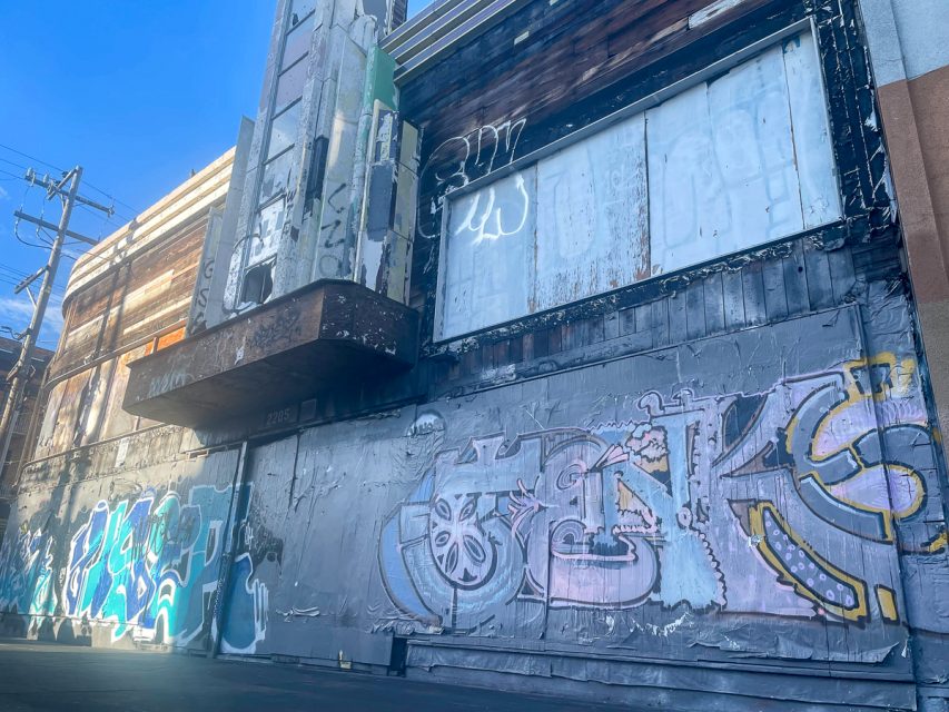An exterior wall with graffiti and weathered paint on an old building under a clear blue sky.