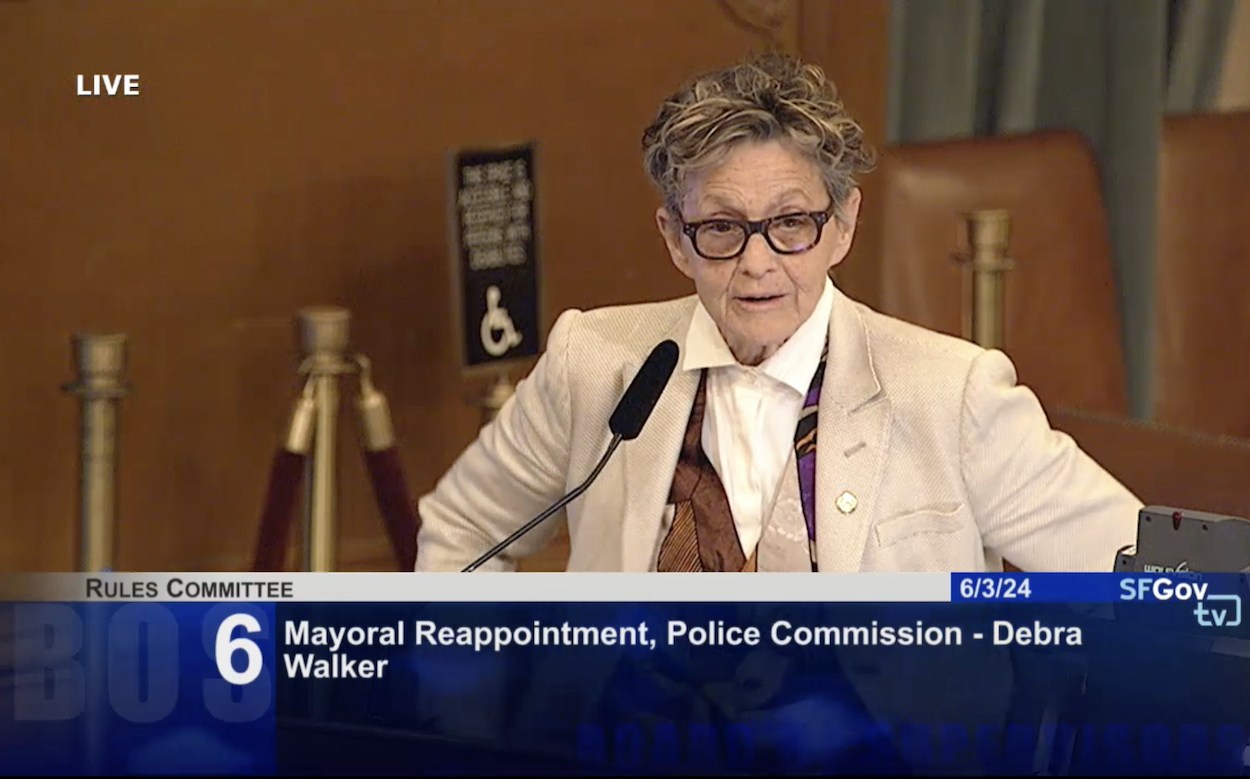 An individual is speaking at a podium during the Rules Committee meeting shown on SFGov TV. The agenda item displayed is number 6: Mayoral Reappointment, Police Commission - Debra Walker.