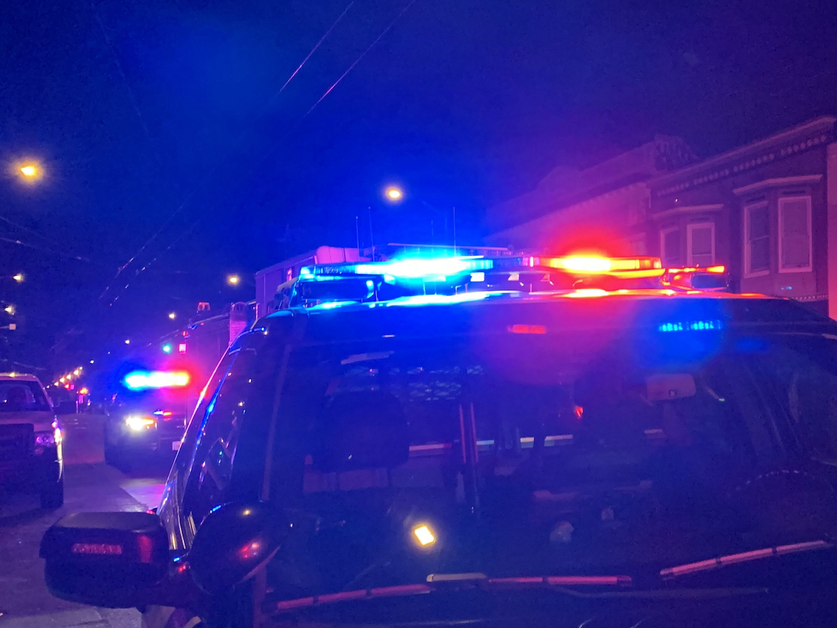A row of police cars with flashing red and blue lights parked on a city street at night.