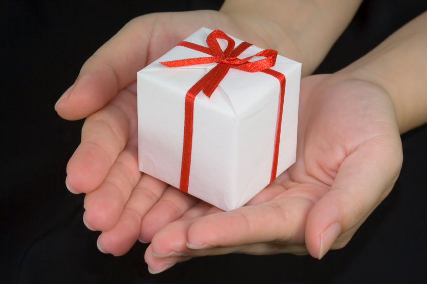 A person holds a small white package wrapped in a red bow