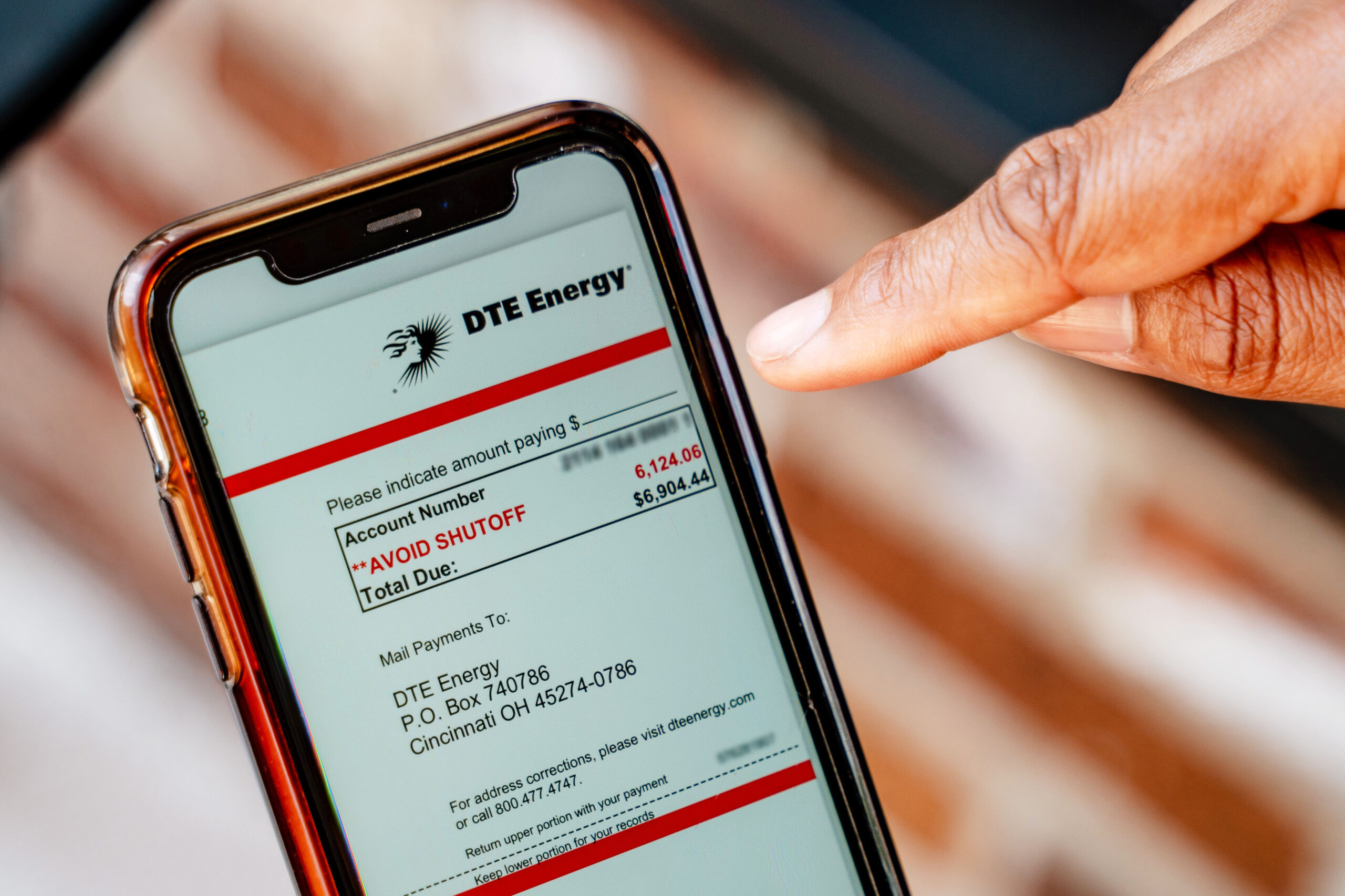 Image of person scrolling a redacted DTE bill on a cell phone.