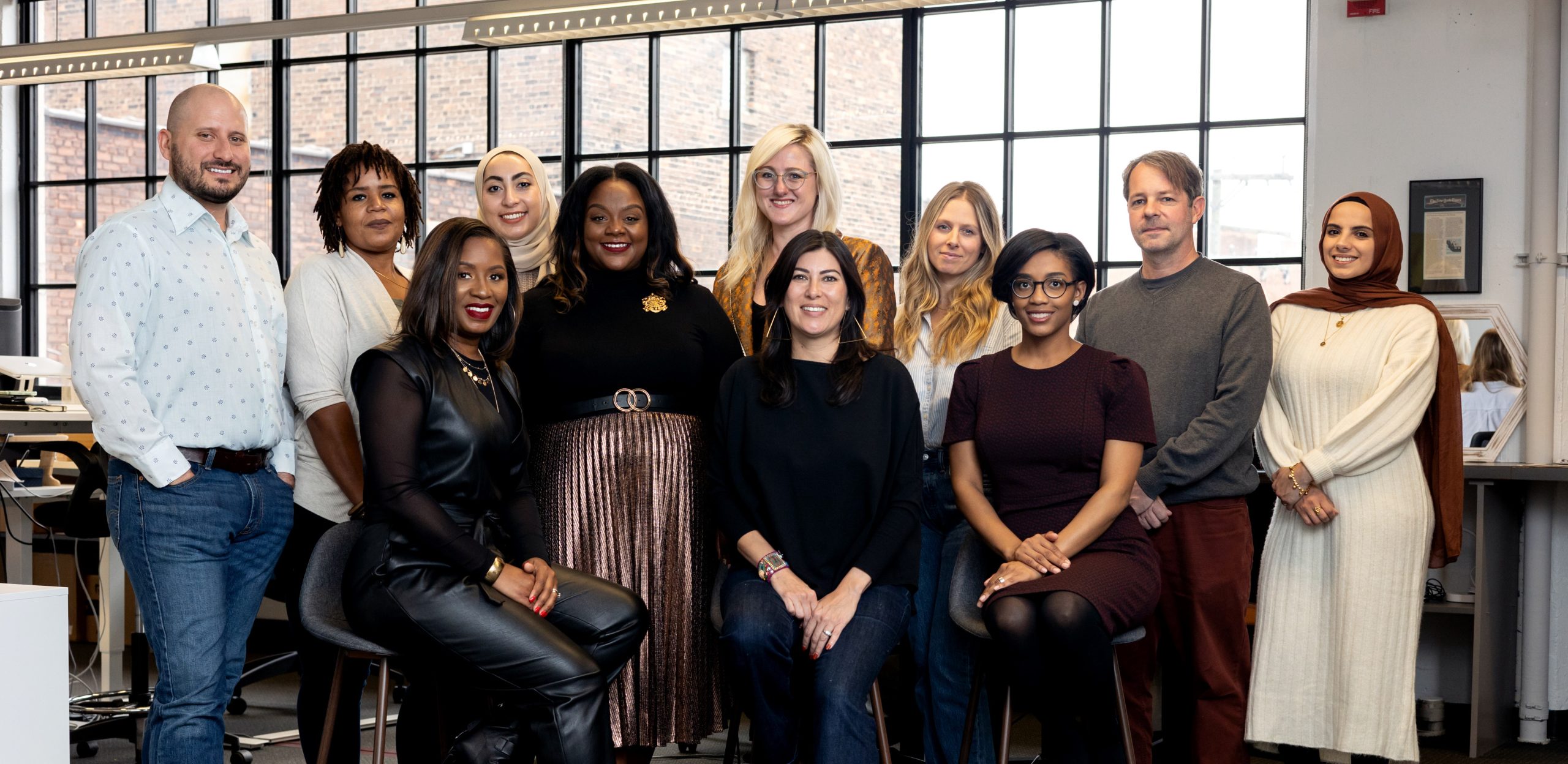 Eleven people smiling for the camera, in an office with a large window.