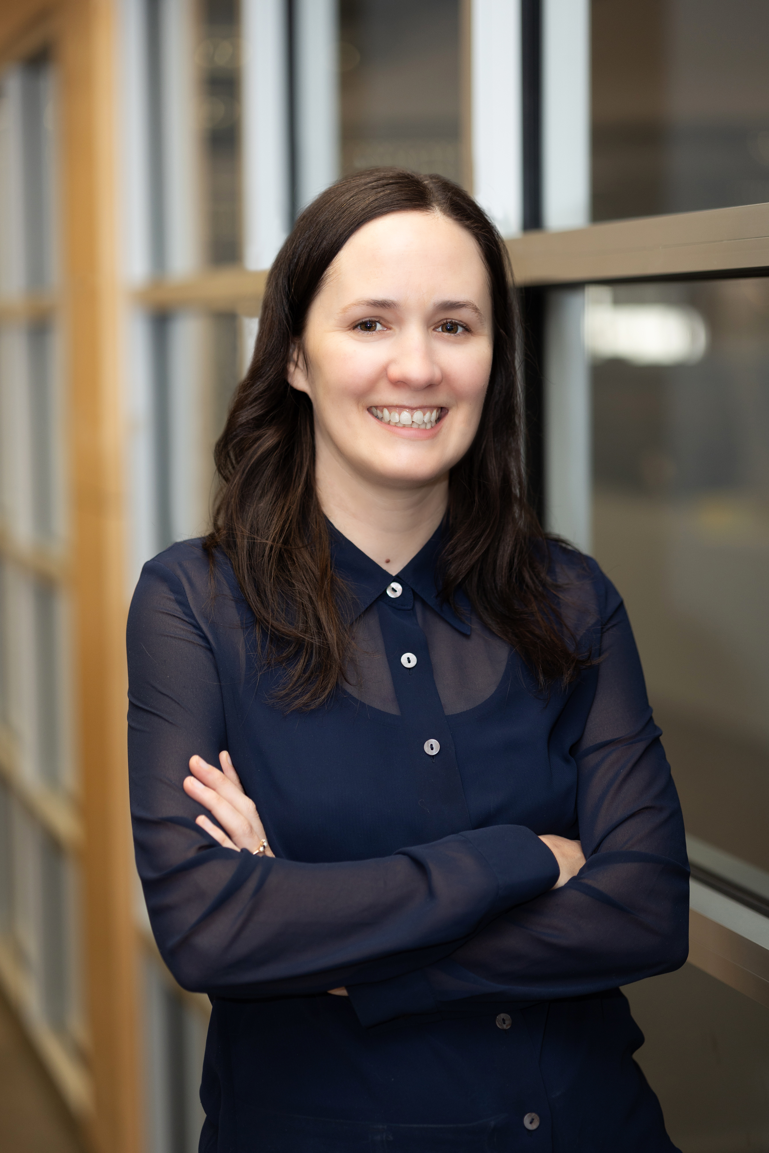 White woman with dark hair with her arms folded and wearing a sheer, navy blue button-up blouse.