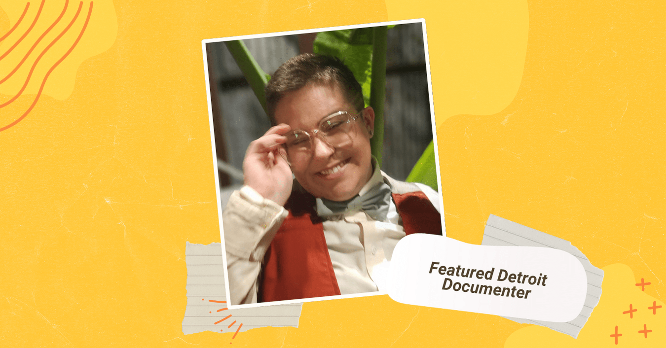 A white person smiles in front of a large green leafy plant. They are wearing a burnt orange vest, cream button-up and a green bow tie and large-framed glasses.