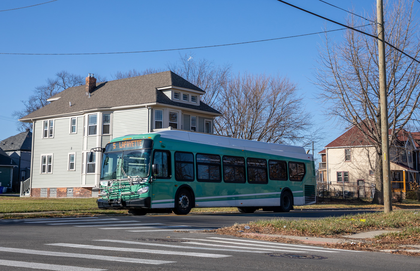 A green bus on a residential street. The signage on the bus reads “5 Lafayette.”