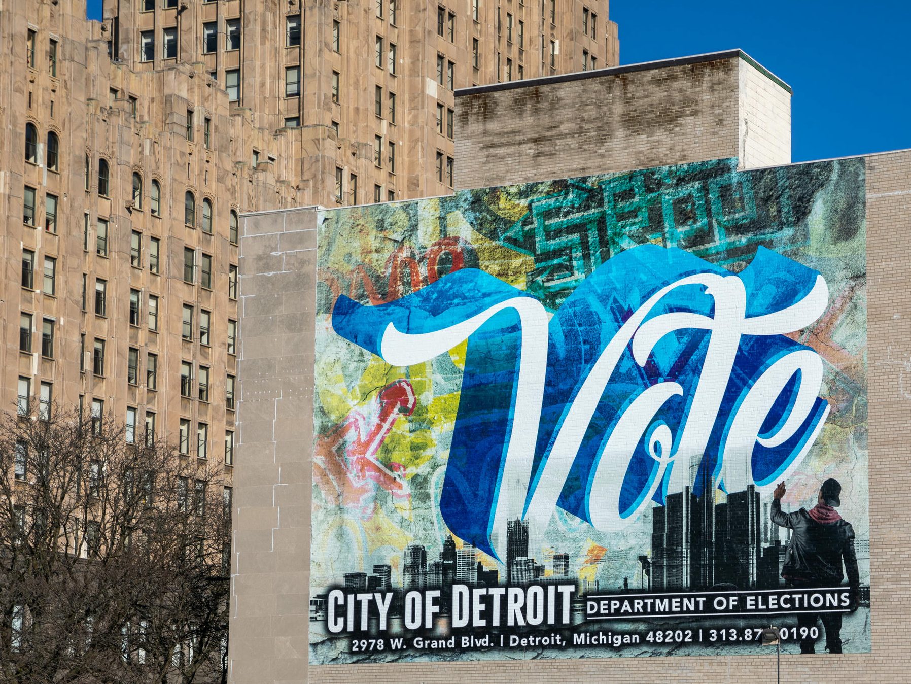 A mural painted on a wall spells out “vote” in white script in front of a blue background.