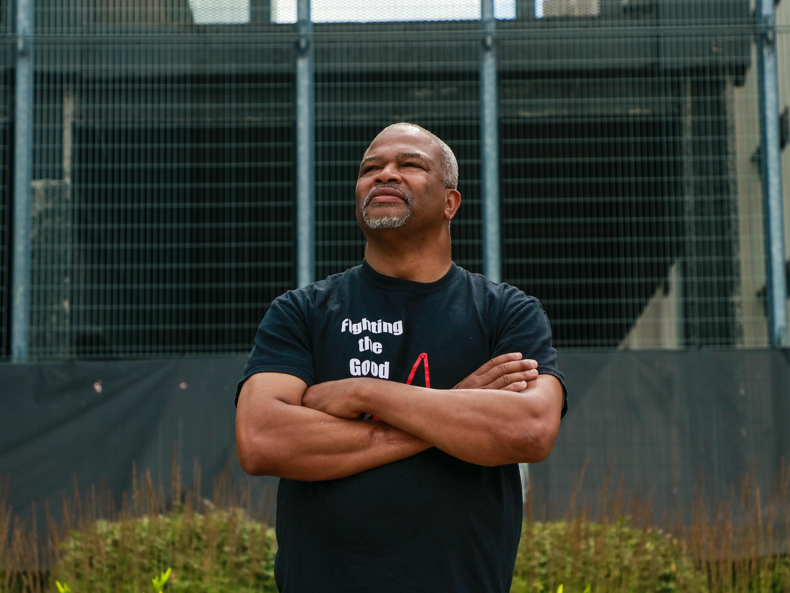 A Black man stands with his arms folded looking up and into the distance.