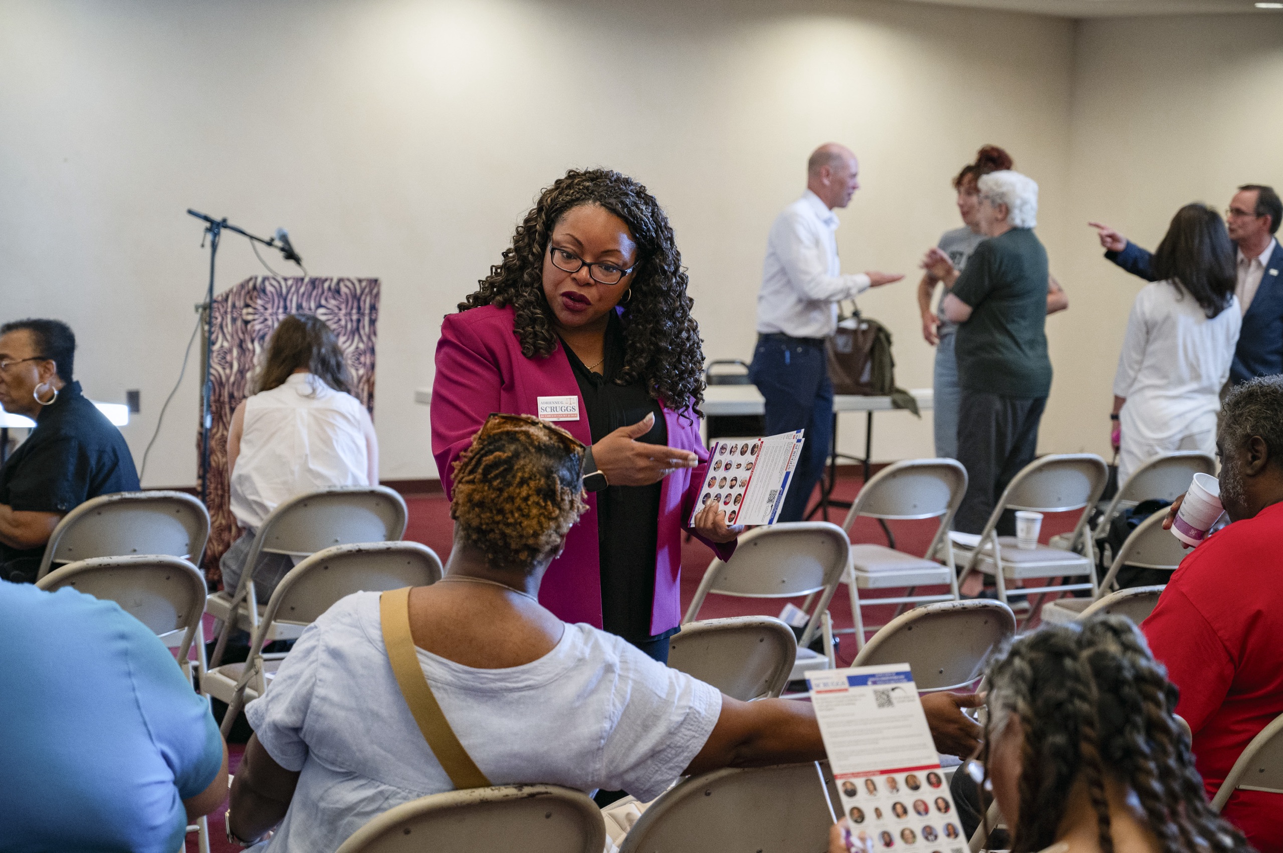 A woman in a magenta blazer engages in a conversation with seated attendees at an event.