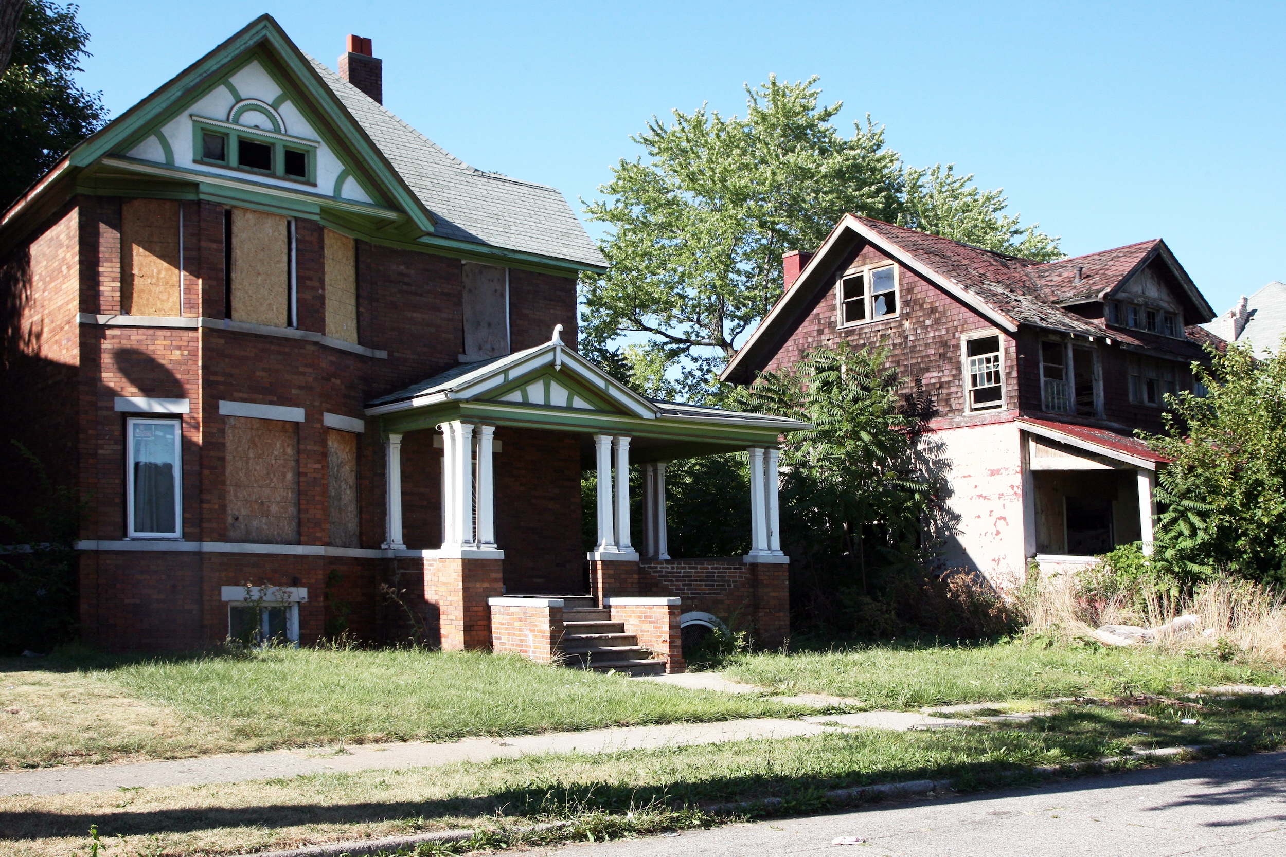 Two brick homes with boarded up or broken windows.