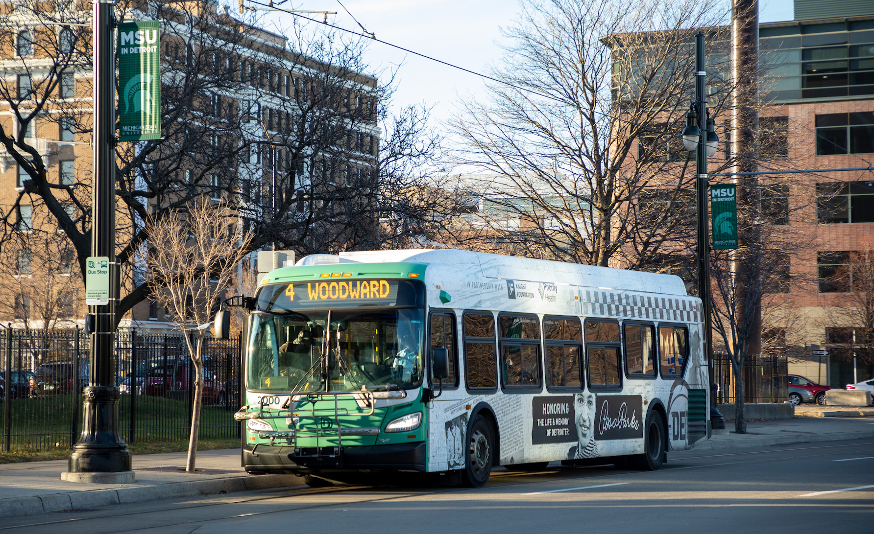 Green and white bus on the side of the road. Screen on the front says “4 Woodward.”