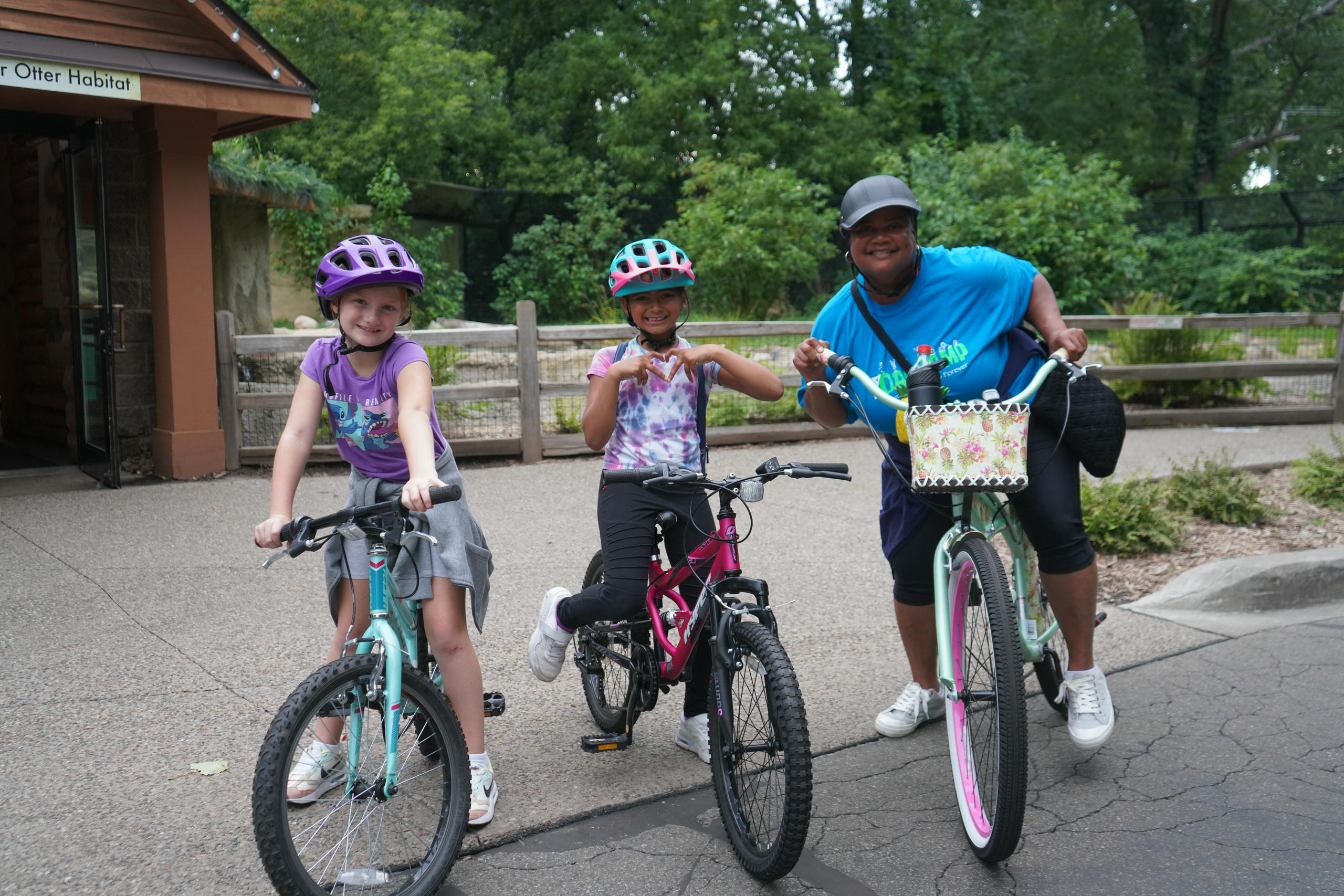 Two children and a woman wearing helmets stand on their bikes in a forest area.