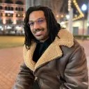 Black man with glasses wearing a brown coat.