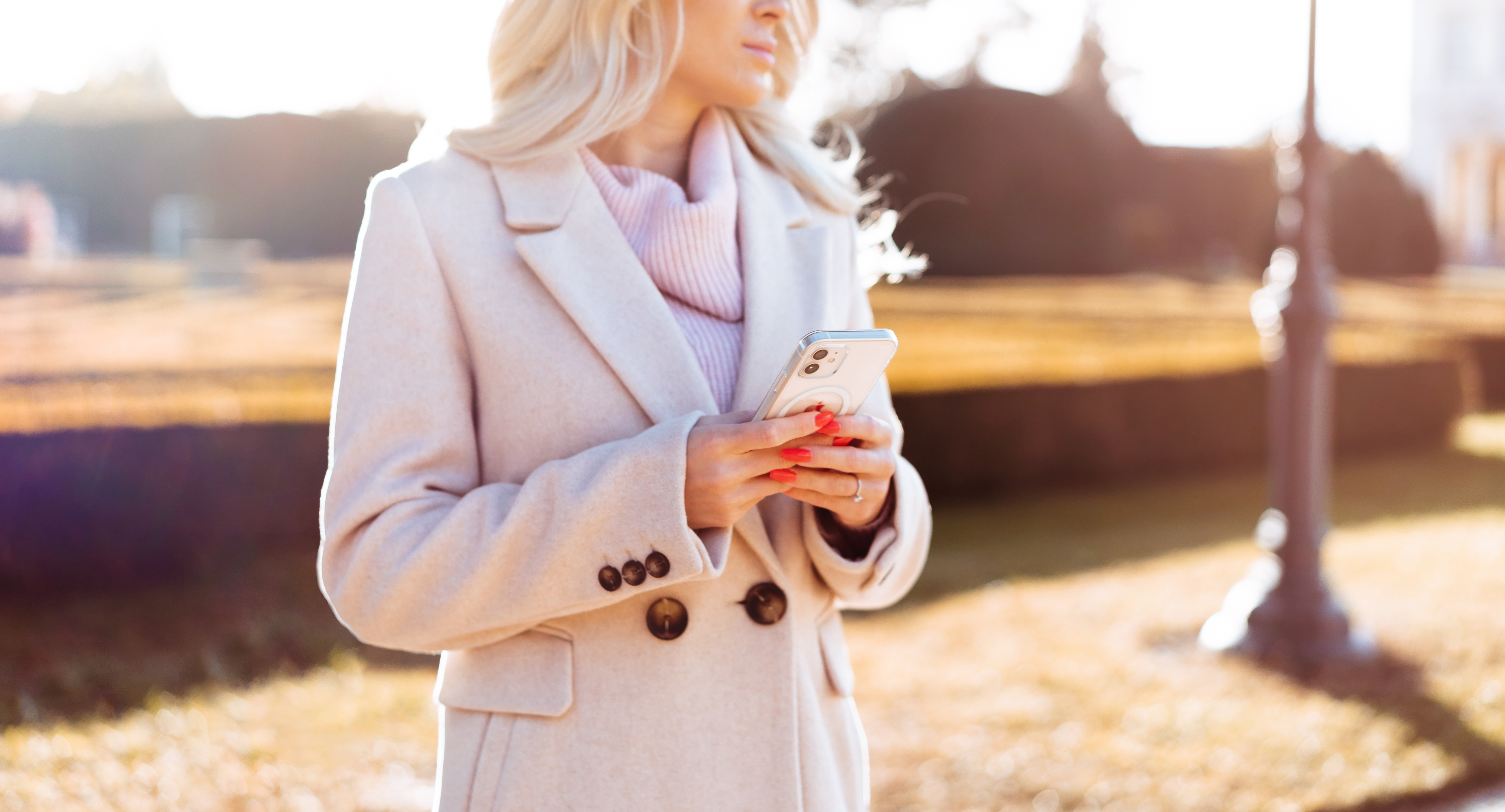 Woman in Coat Holding Her White Smartphone in Hands During Sunny Fall Free Photo