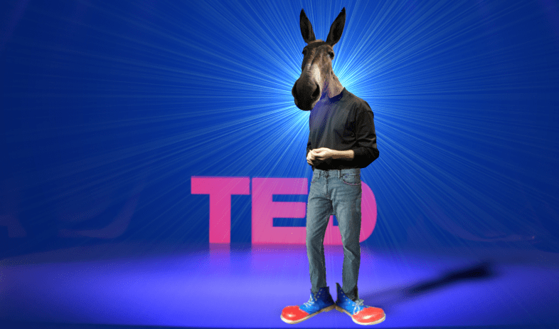 A humanoid figure standing to the fore of a TED stage; he wears Steve Jobs’s signature turtleneck and bluejeans, but he is also wearing clown shoes. His head has been replaced by a donkey’s head.