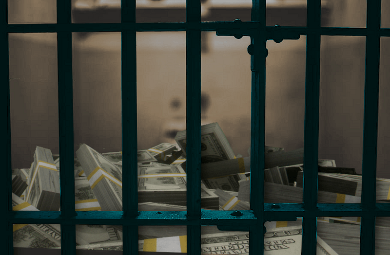 A jail cell, seen through the bars. Bundles of US $100 bills are piled up on the floor of the cell.