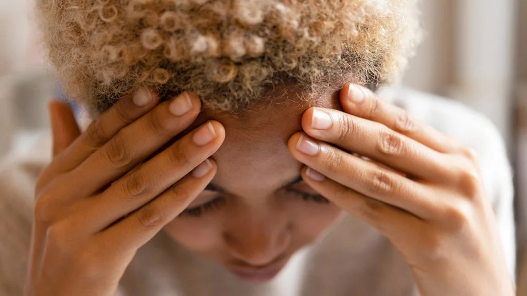 a woman holding her forehead as she has pain there from a basilar migraine