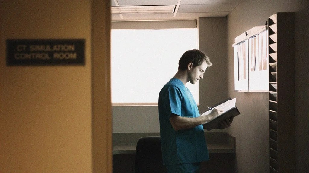 a doctor wearing blue scrubs is reading reports while standing in hospital ward