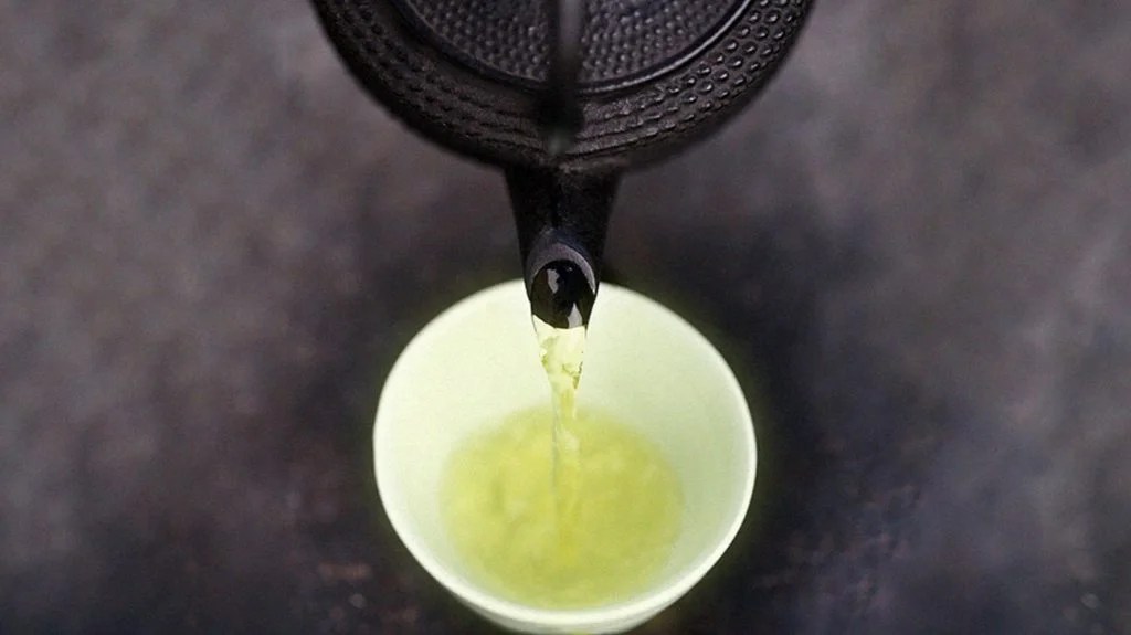 A teapot pouring green tea into a cup.