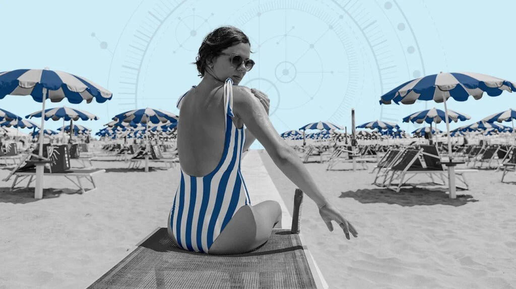 Adult female sitting on a sun lounger on a beach looking back over her right shoulder 