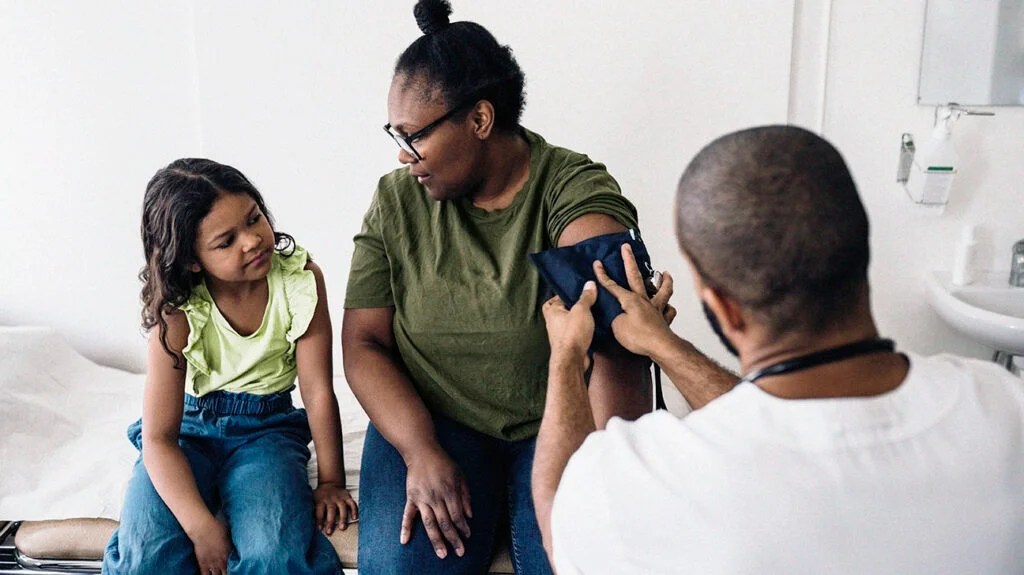 Mother talking with daughter while male doctor measures blood pressure or hypertension