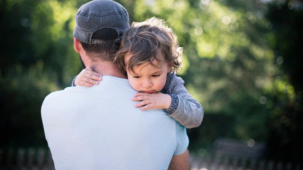 2 year old being held in dad's arms while looking down representing lymphoblastic leukemia