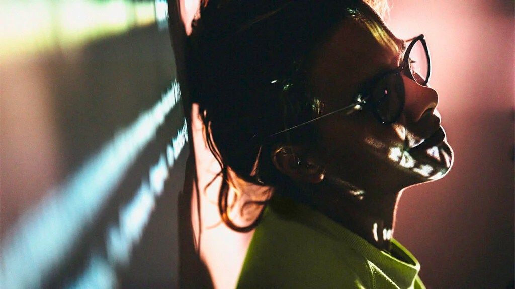 Tired female professor in hipster glasses is standing against a projector wall