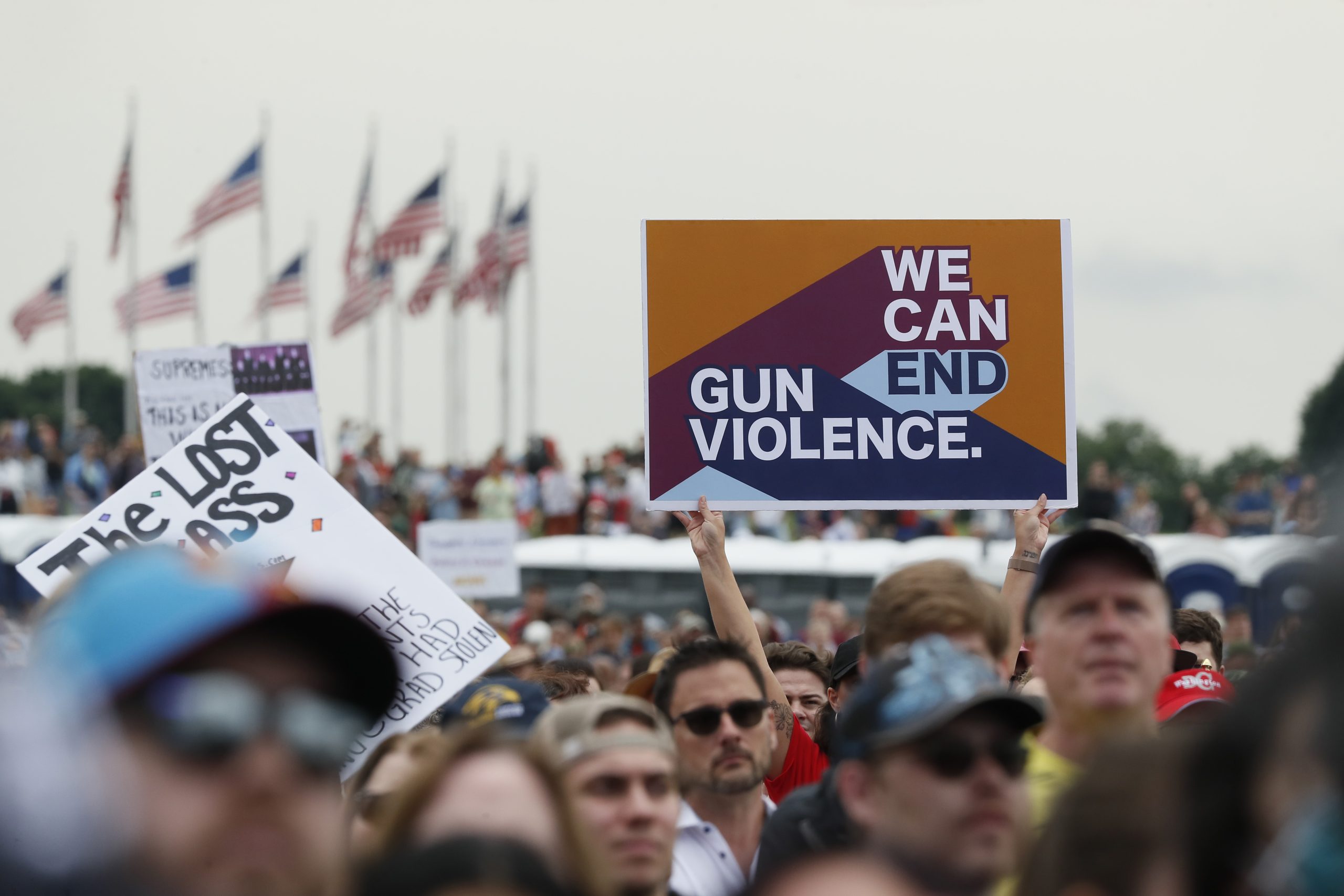 A crowd of people at a gun violence protest, their faces are out of focus. One sign that reads 'We Can End Gun Violence' is held up above the crowd.
