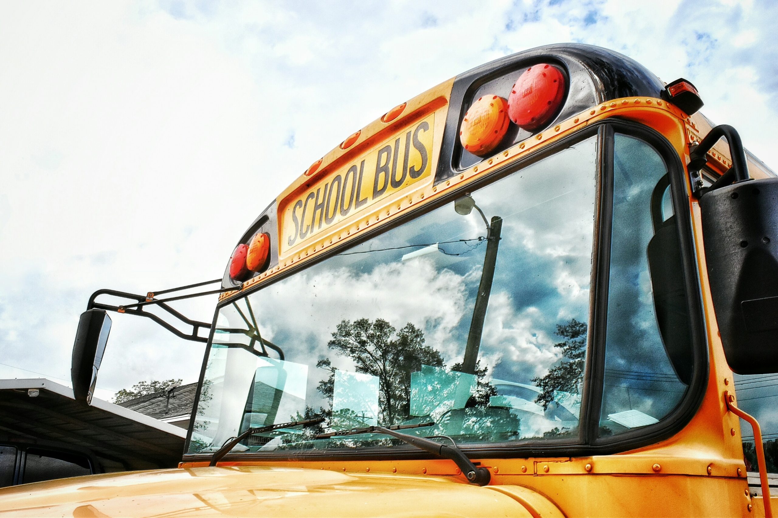 A yellow school bus up close to the camera, with a slightly clouded blue sky visible behind it.