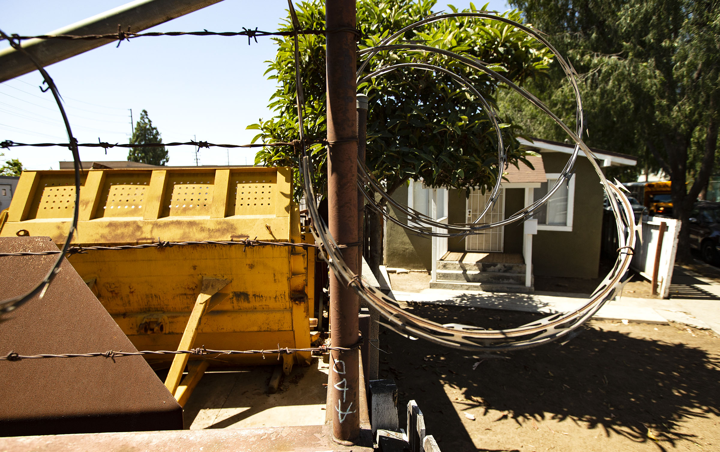 A barbed wire barrier hangs over a wall separating an industrial business and the residential yard of the home where Nalleli Garrido lives.